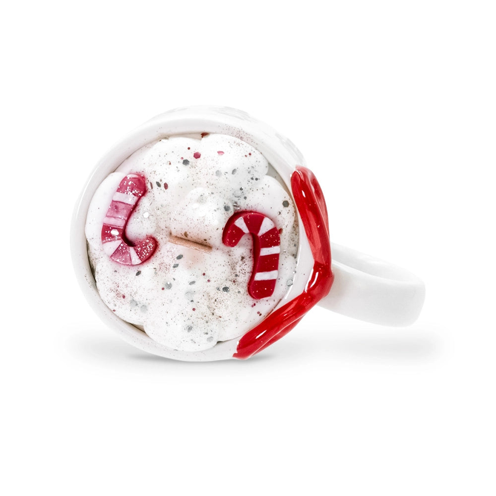 Vue de dessus de la bougie mug casse noisette, décor de cire blanche pailletée, deux cannes de Noël rouge et rose, nœud rouge, Les Fées Mères