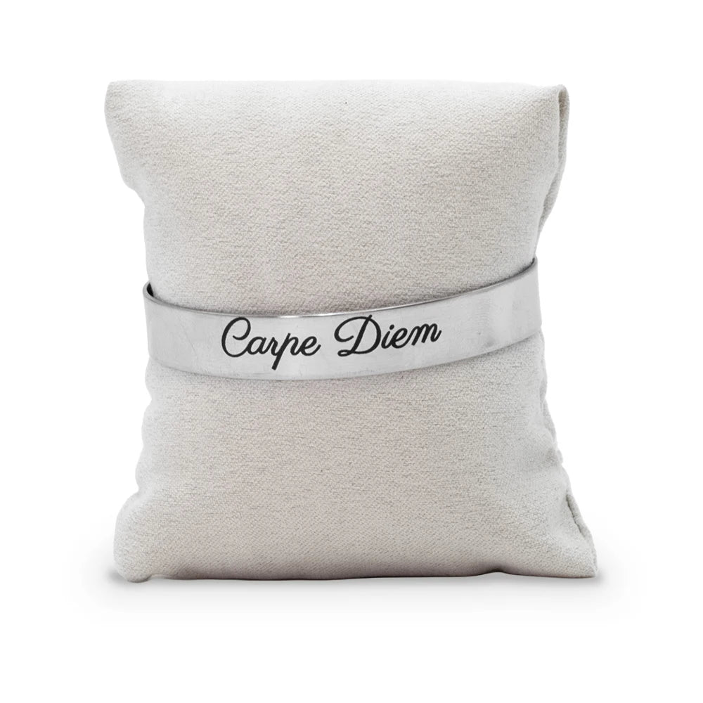 Bracelet jonc gravé Carpe Diem en écriture manuscrite noire sur acier inoxydable, présenté sur un coussin en tissu beige, Les Fées Mères