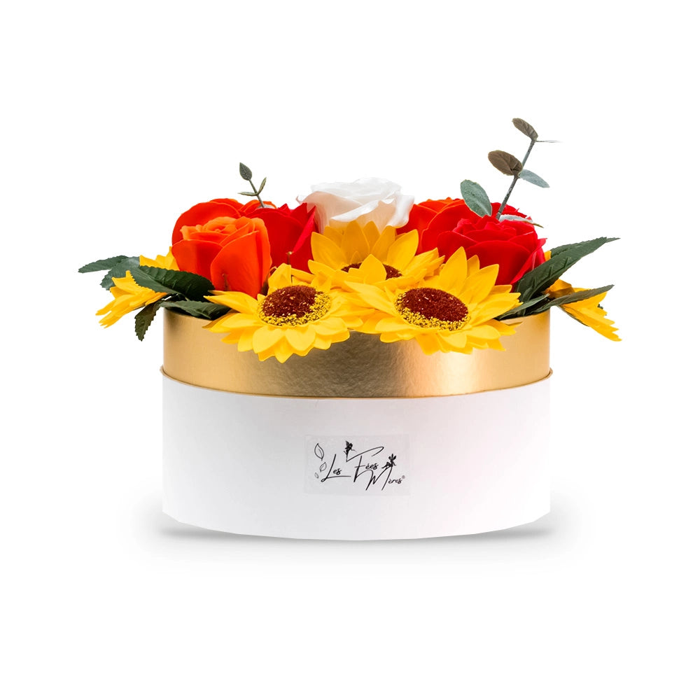 Composition en fleurs de savon tournesols et roses Les Fées Mères, tournesols jaunes, roses rouges, orange et blanche et brins d'eucalyptus dans une boîte ronde blanche au liseré cuivre, logo de la marque