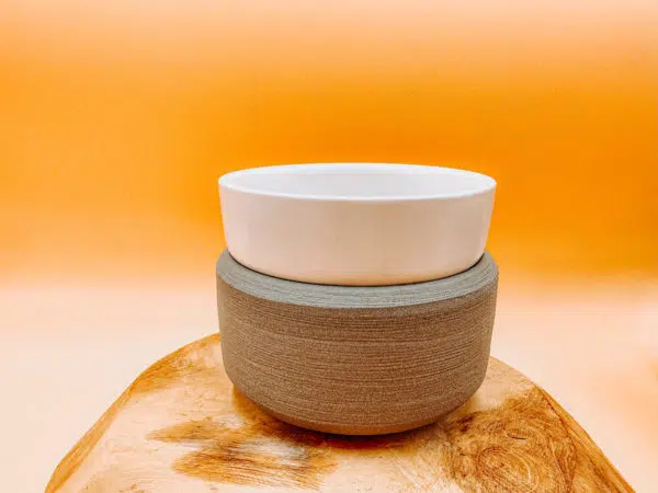 Cette photo représente un diffuseur électrique 2 en 1 gris et blanc. Il permet de diffuser le parfum contenu dans les fondants Les Fées Mères, mais aussi de fondre et diffuseur la senteur d'une bougie. Il est blanc et gris et s'allie parfaitement dans tous type d'intérieur.