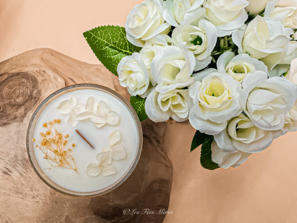 Cette image représente la bougie fleurie artisanale parfumée mèche en bois de hêtre. Elle est d'un design simple et épuré de couleur blanche. Cire de soja sans OGM et véritable parfum de Grasse.