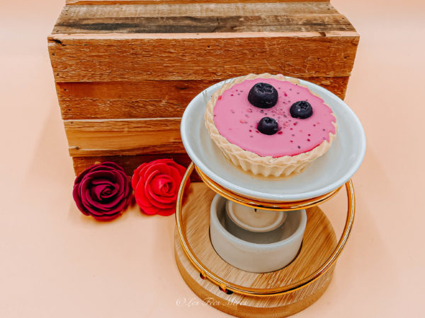 Tartelette parfumée cassis freesia. Présenté sur une tablette en bois. Les deux tartelettes sont composées de cire de colza rose ainsi que de 3 cassis en cire parfumée également. Vu sur un brûle parfum.
