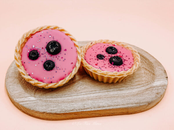 Tartelette parfumée cassis freesia. Présenté sur une tablette en bois. Les deux tartelettes sont composées de cire de colza rose ainsi que de 3 cassis en cire parfumée également.