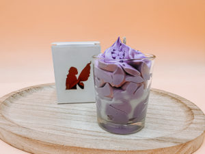 Cette image représente la bougie gourmande violette et sa boîte blanche. C'est une bougie chantilly.