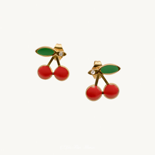 Cette photo représente les boucles d'oreilles puces cerises. Nous pouvons observer une paire de boucle d'oreille identique représentant des cerises sur une base doré, deux boules rouge pour le fruit, une forme de feuille couleur verte et un petit strass à coté de la feuille.